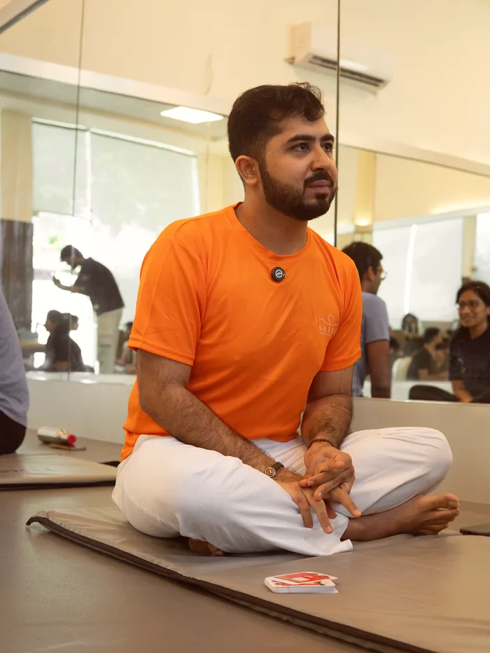 The teacher seated cross-legged, hands resting, watching the circle