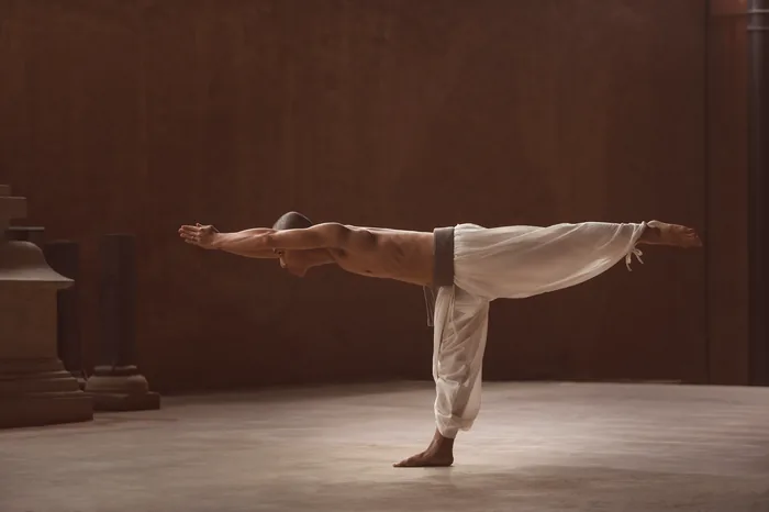 A practitioner level in warrior three in a warm stone hall