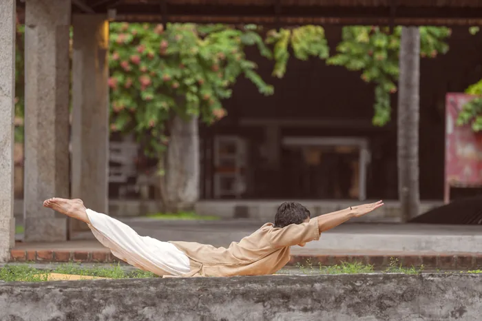 A practitioner in locust pose along an open stone colonnade