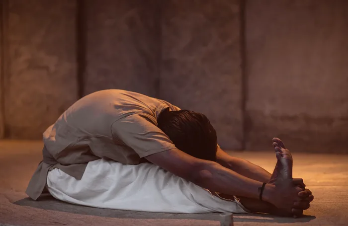 A practitioner folded flat over her legs on a dark stone floor
