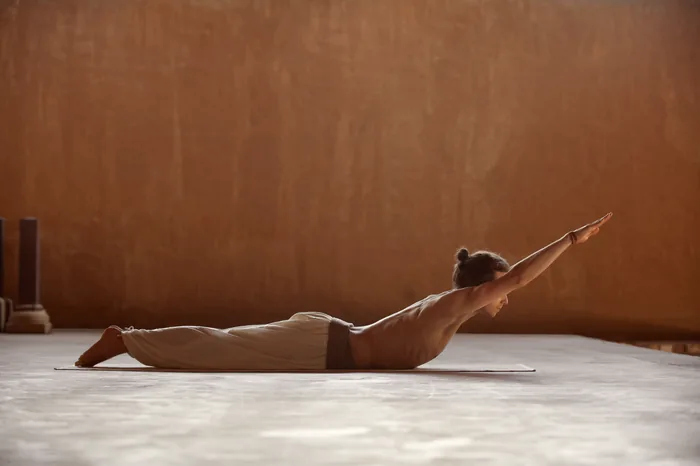 A practitioner lifting into locust pose against an ochre wall