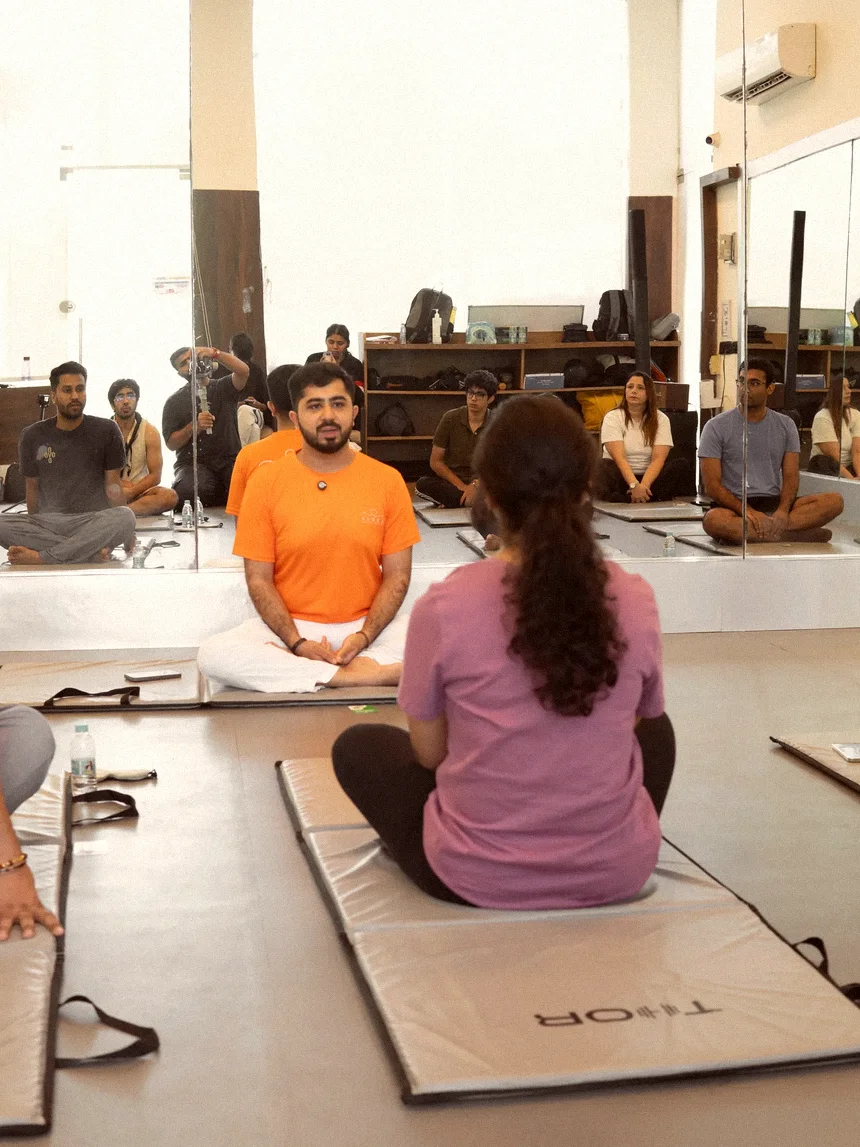 A full room seated on mats, the teacher mid-sentence at the front