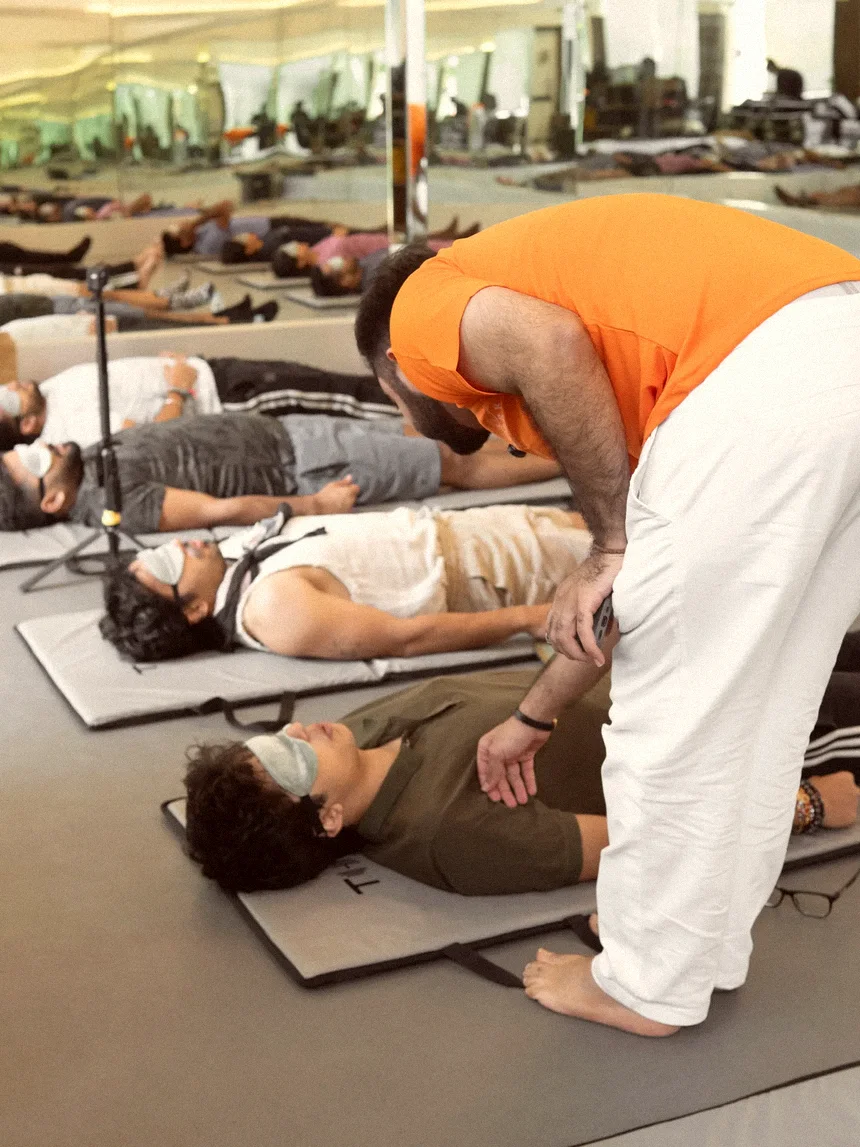 A facilitator moving between people lying masked on mats, guiding a round of breathwork