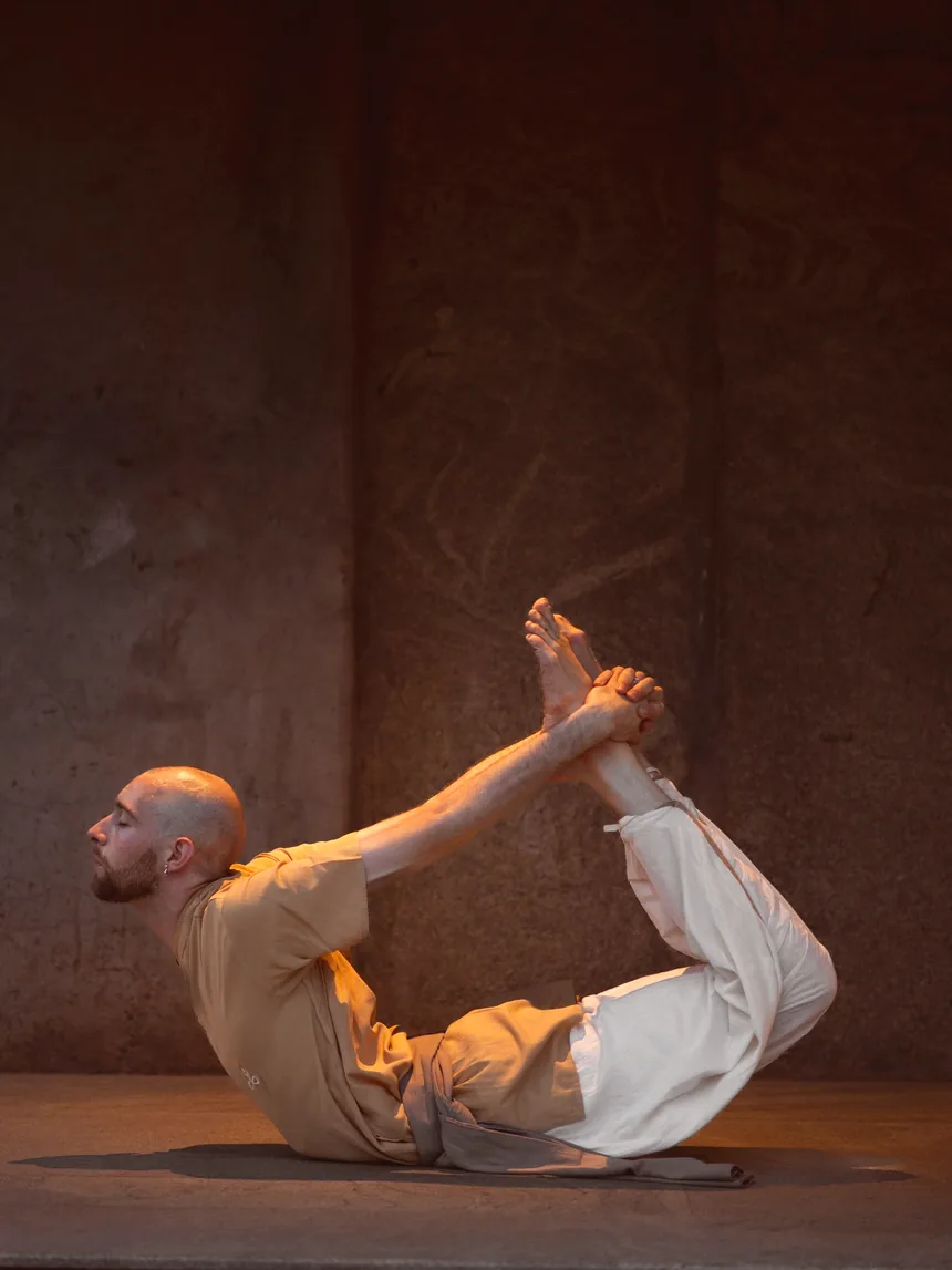 A practitioner holding bow pose in a warm stone hall
